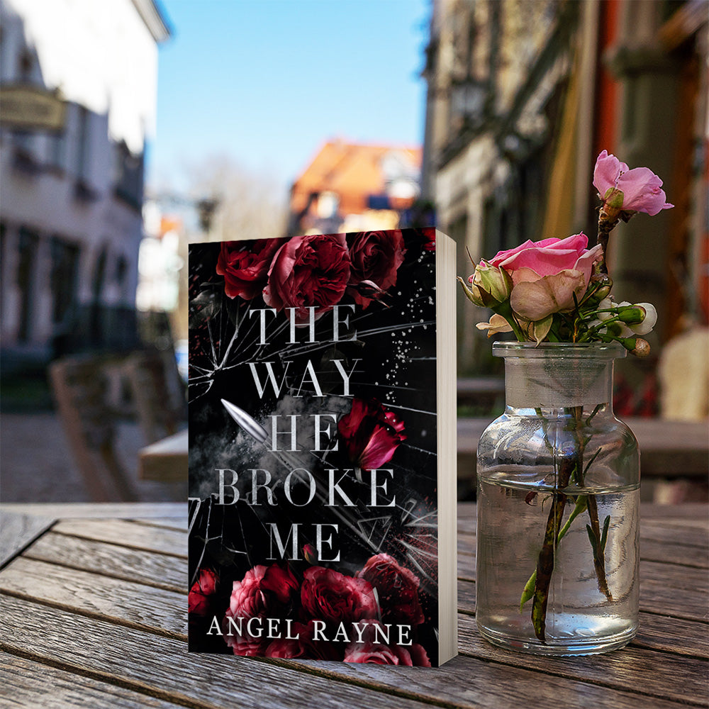 Book titled 'The Way He Broke Me' by Angel Rayne with a pink rose in a glass vase on a wooden table.